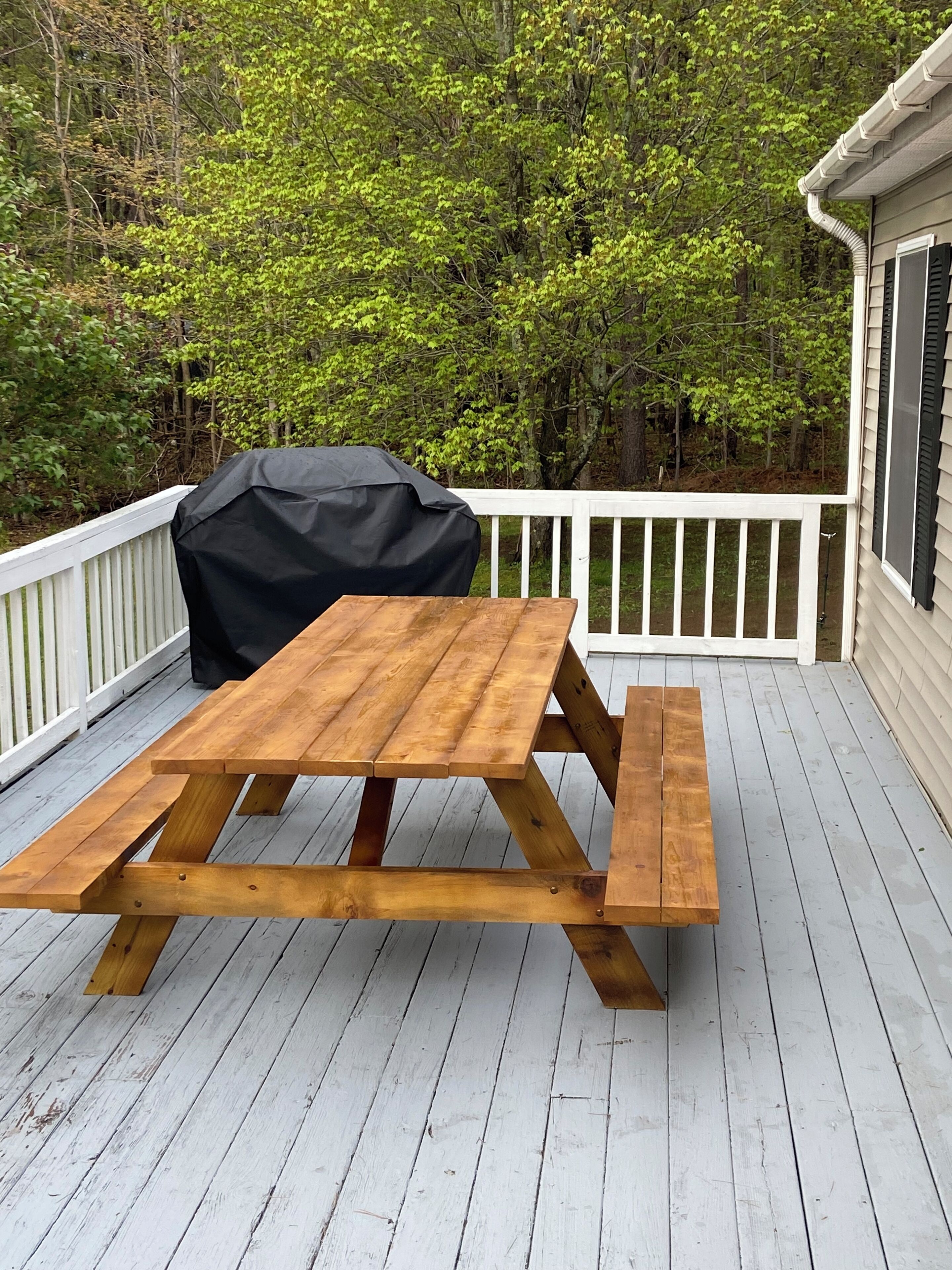 A wooden picnic table with benches on a wooden deck, surrounded by white railings and trees.
