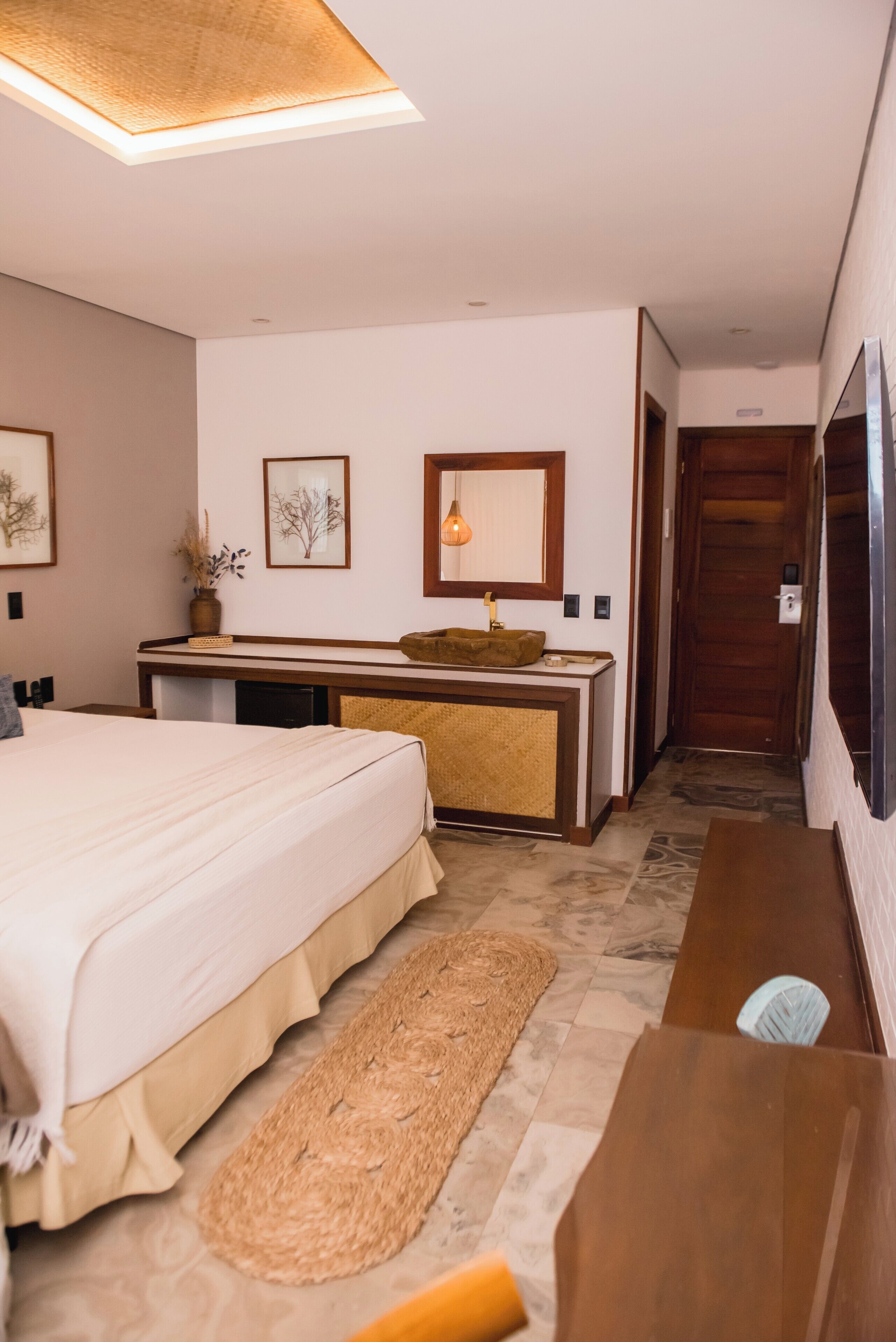 Een hotelkamer met een bed, een bureau, een spiegel en een deur die naar een andere kamer leidt.