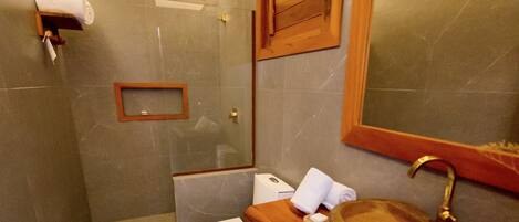 A compact bathroom with a marble floor, a wooden vanity, a white toilet, a glass shower enclosure, and a mirror above the sink.