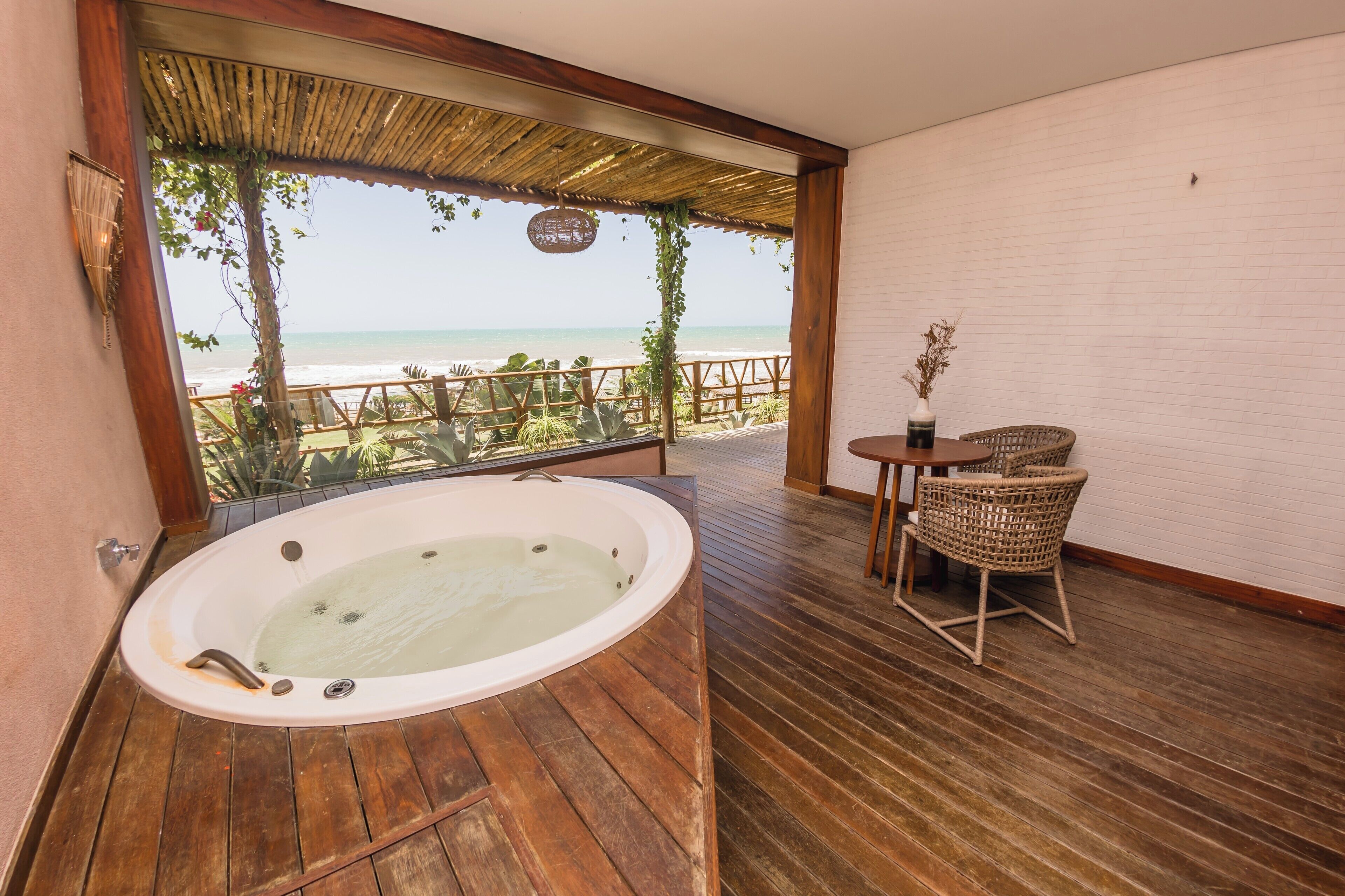 Una habitación con piso de madera, una bañera grande, sillas de mimbre y vista a la playa.
