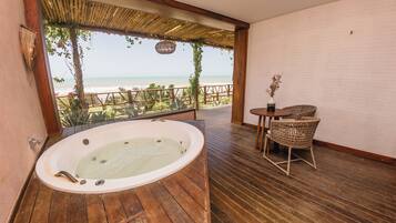 Una habitación con piso de madera, una bañera grande, sillas de mimbre y vista a la playa.