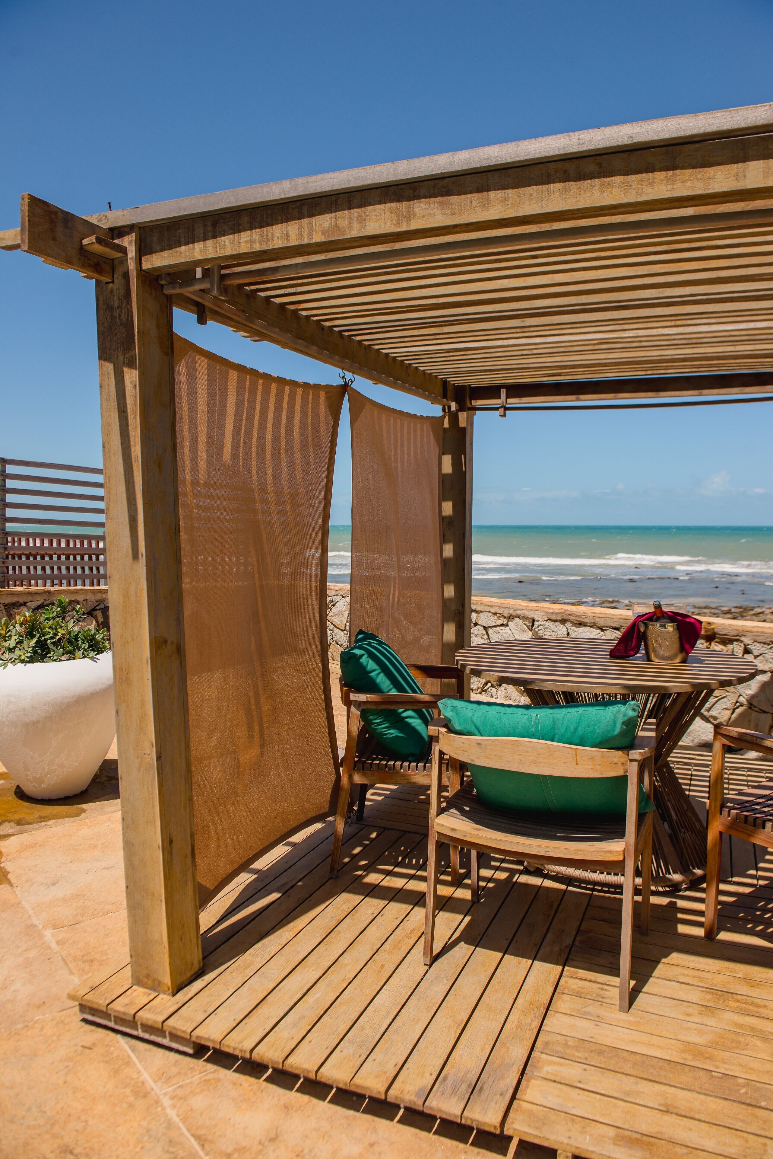 Une terrasse en bois avec un espace salon couvert donnant sur la plage.