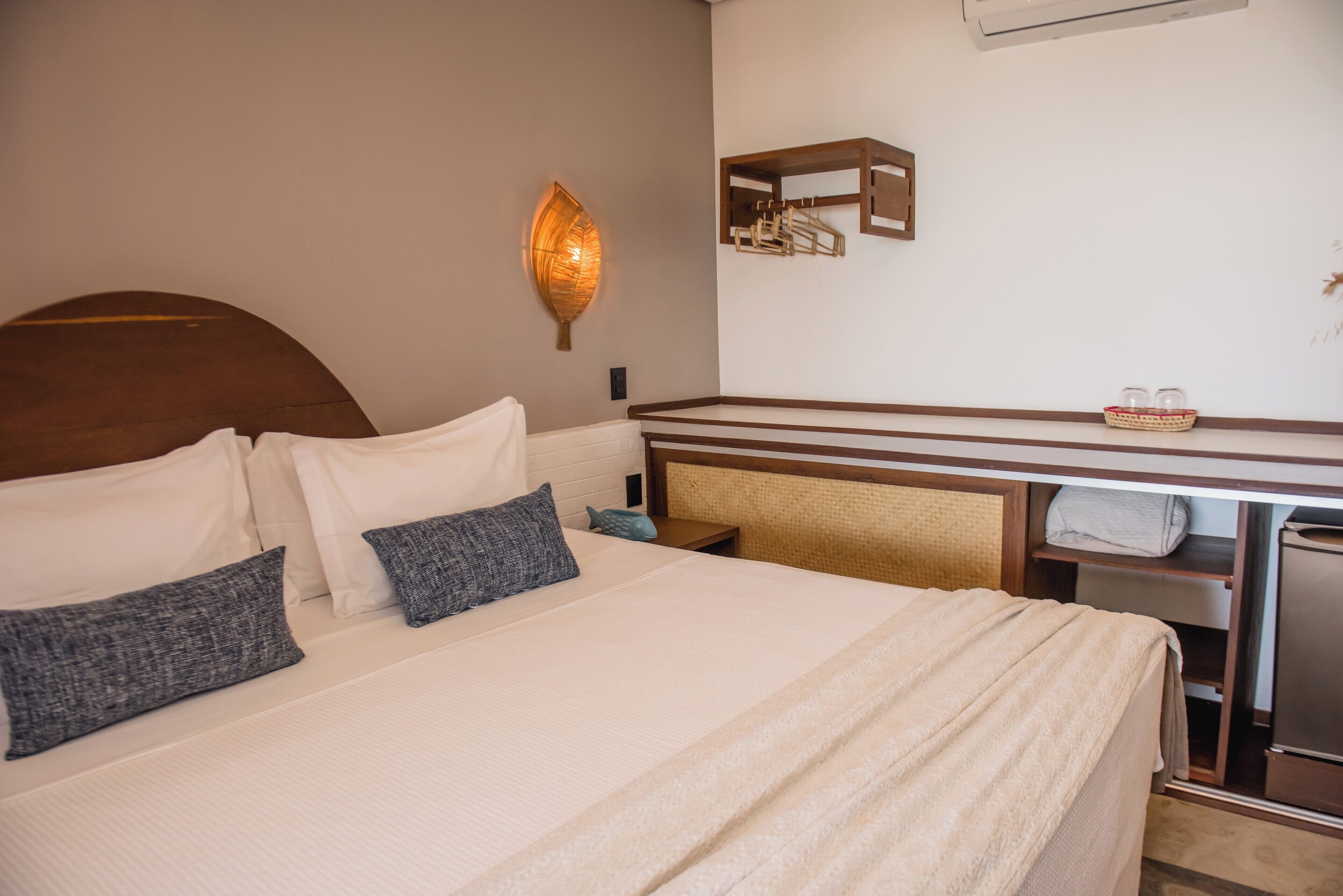 A neatly made bed with pillows, a bedside table, a wall-mounted light fixture, and a small shelf with towels.
