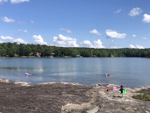 A lake with a rocky shore and a forested area in the background. - Lake Wedowee Bass House (Lineville)