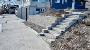 A two-story house with a garage, a driveway, and a stone retaining wall with steps leading up to the house. - Spacious & Private Suite in a Central location (Arvada)