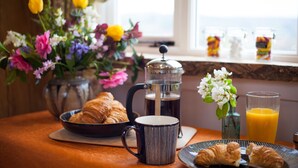 Une table mise pour le petit-déjeuner avec des croissants, une cafetière, une tasse, un vase de fleurs et un verre de jus d’orange.