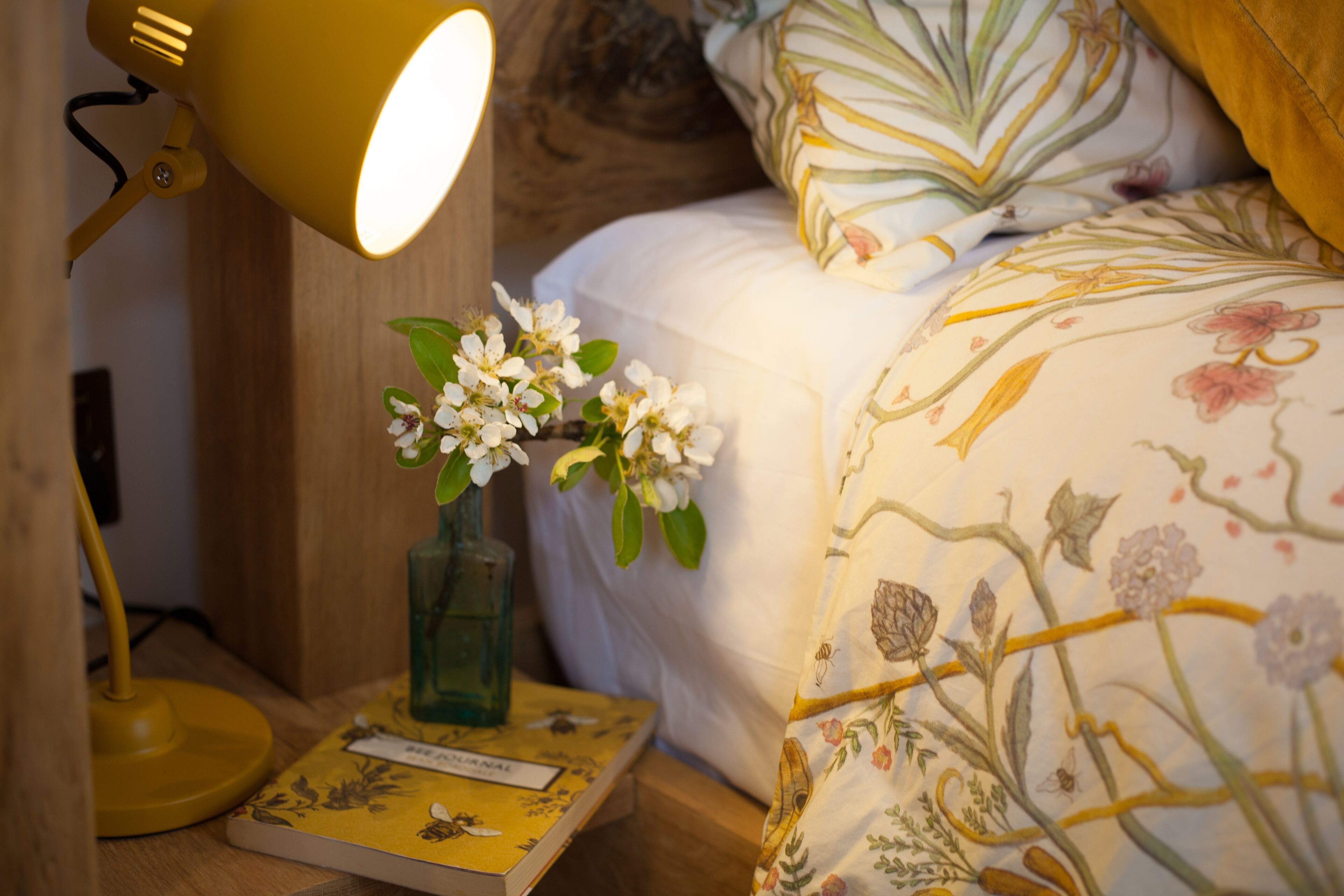 A bedside table with a lamp, a book, and a vase with flowers.