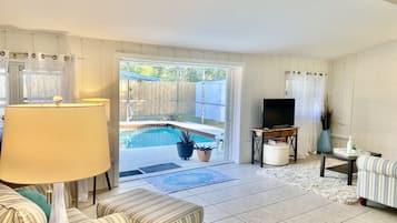 Relax in this inviting living room with a large window overlooking a backyard pool and lush greenery.
