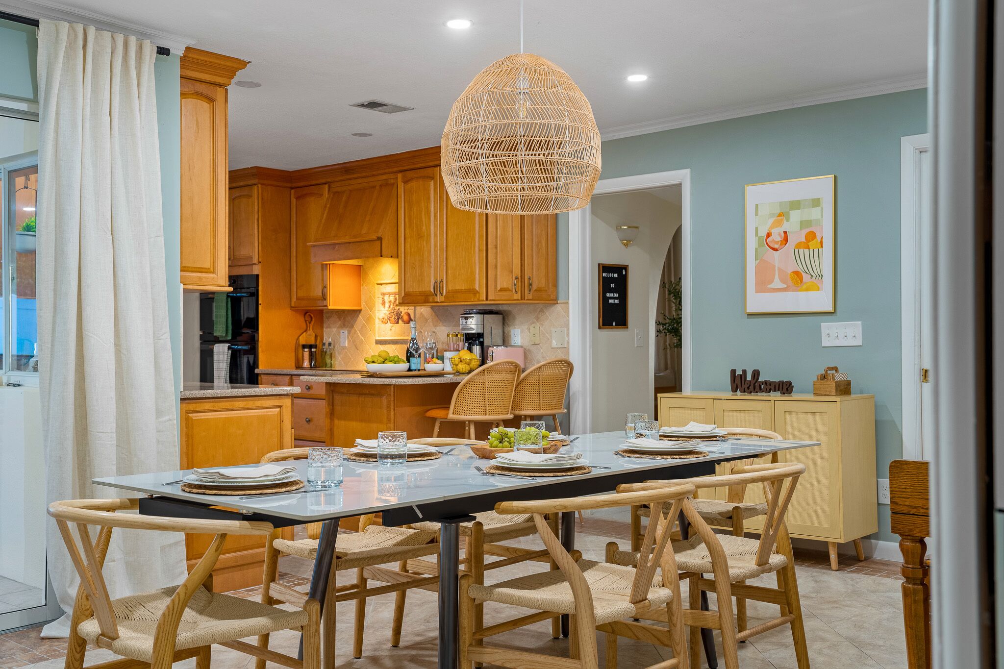Une cuisine moderne avec des meubles en bois, une table à manger pour six personnes et un luminaire suspendu.