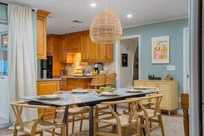 A modern kitchen with wooden cabinets, a dining table set for six, and a hanging light fixture. - Heated salt water pool Spacious 4BR,3BR (Dunedin)