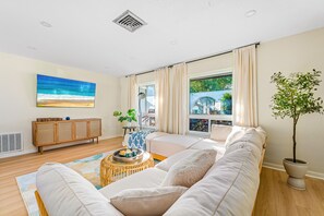 A modern living room with a large window, a sofa set, a wooden cabinet, and a potted plant. - Heated salt water pool Spacious 4BR,3BR (Dunedin)