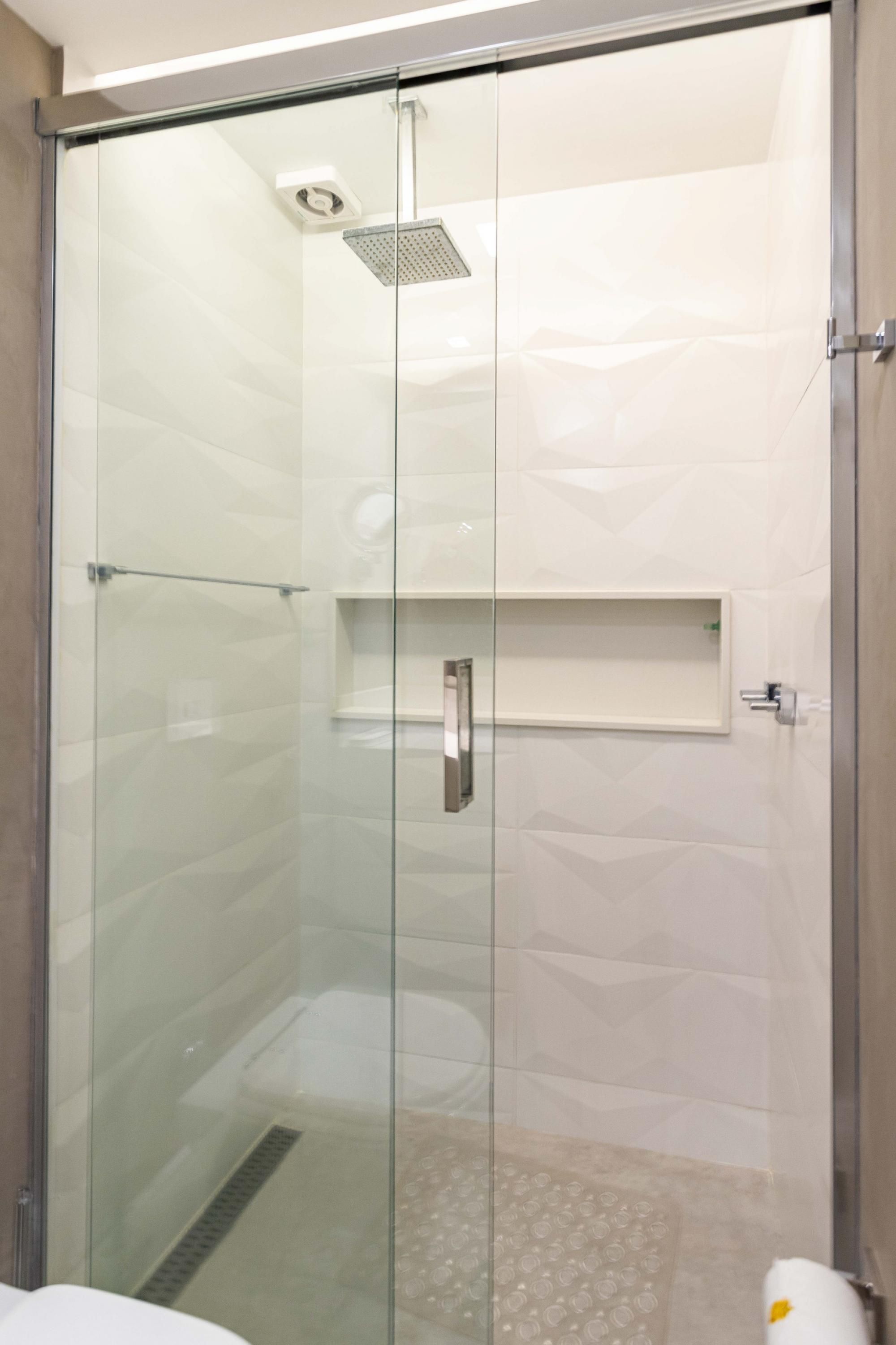 A glass-enclosed shower with a handheld showerhead, a towel rack, and a shelf above the shower.