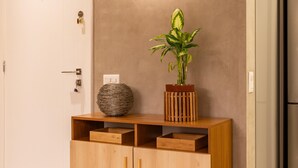 Un meuble en bois avec des tiroirs, un vase et une plante en pot, le tout placé contre un mur sur lequel est fixée une applique.
