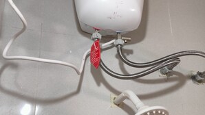 Un cabezal de ducha manual blanco adosado a una unidad de control mural con un interruptor de encendido y una etiqueta roja.