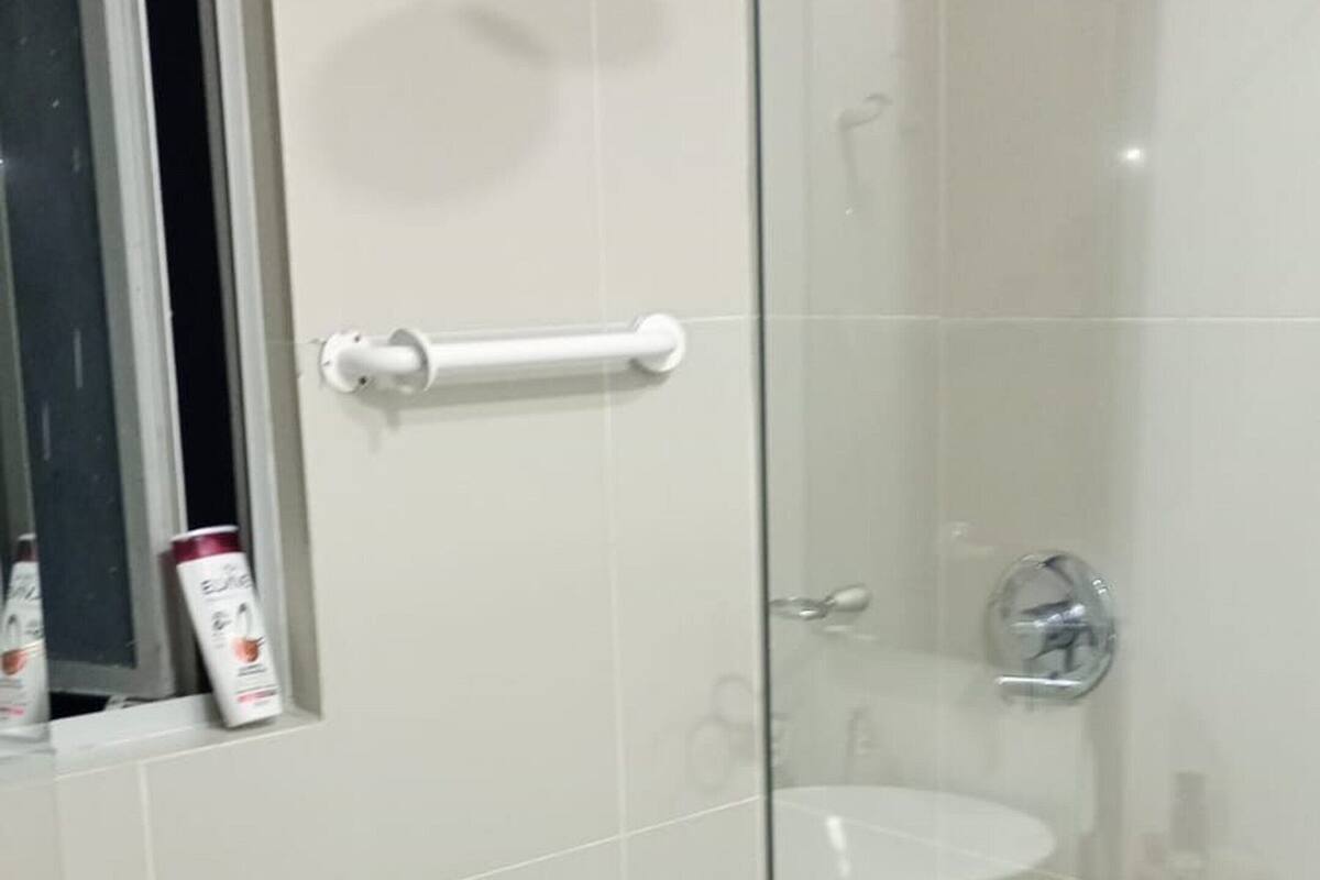 A modern bathroom with a glass shower enclosure, a white sink, and a handrail.