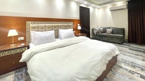 A hotel room with a large bed, two bedside tables with lamps, a grey sofa, and a patterned floor. - Block B - 401 (Agouza)