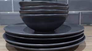 A stack of dark-colored plates and bowls on a wooden surface with a tiled backsplash in the background. - The Old Guest House - R2 (London)