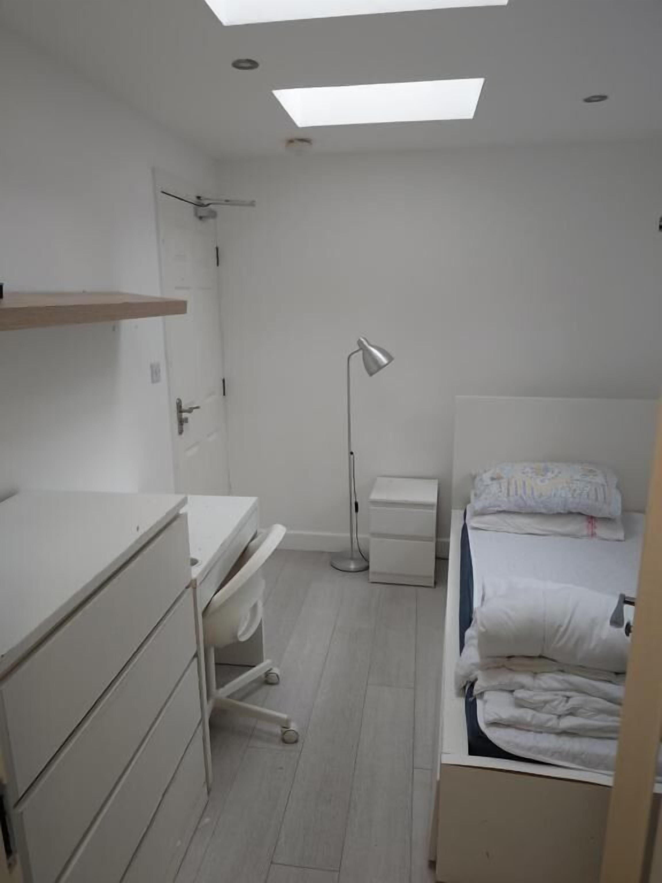 Un dormitorio con escritorio, cama, lámpara de noche y tragaluz.