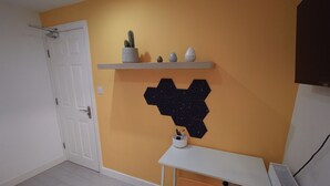 A room with a white door, a small desk with an orange chair, a white radiator, and a wall-mounted shelf with a cactus and two decorative eggs. - The Old Guest House - R2 (London)