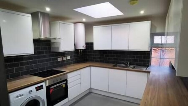 A compact kitchen with a built-in washer and dryer, dark backsplash, and white cabinetry. - The Old Guest House - R2 (London)