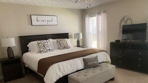 Une chambre à coucher bien rangée, avec un lit, des lampes de chevet, un téléviseur et un panneau décoratif accroché au mur.