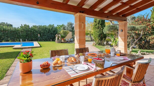 An outdoor dining area with a pool view, wooden furniture, and a variety of breakfast items.