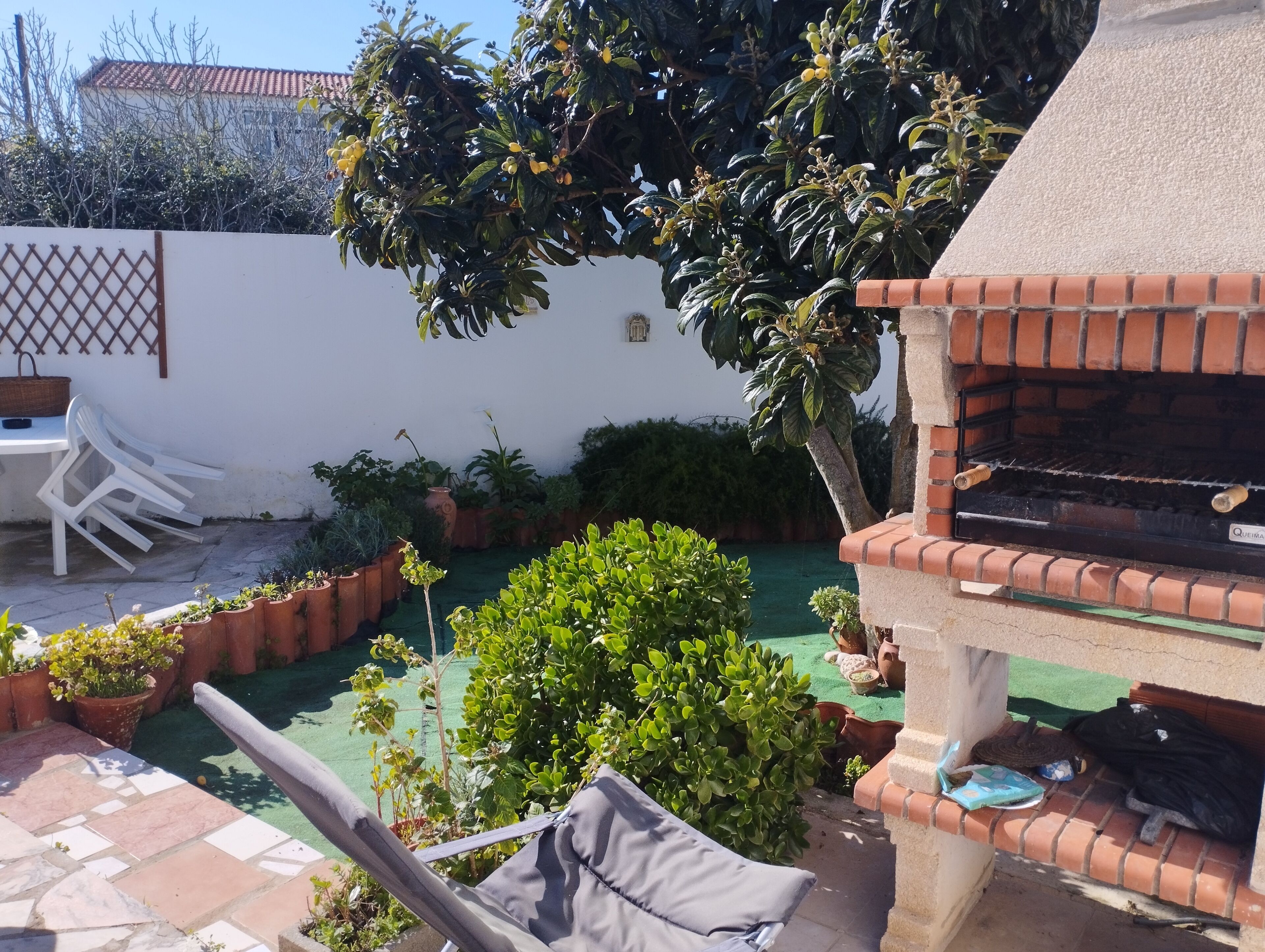 Un patio con una parrilla, plantas en macetas y mobiliario exterior.