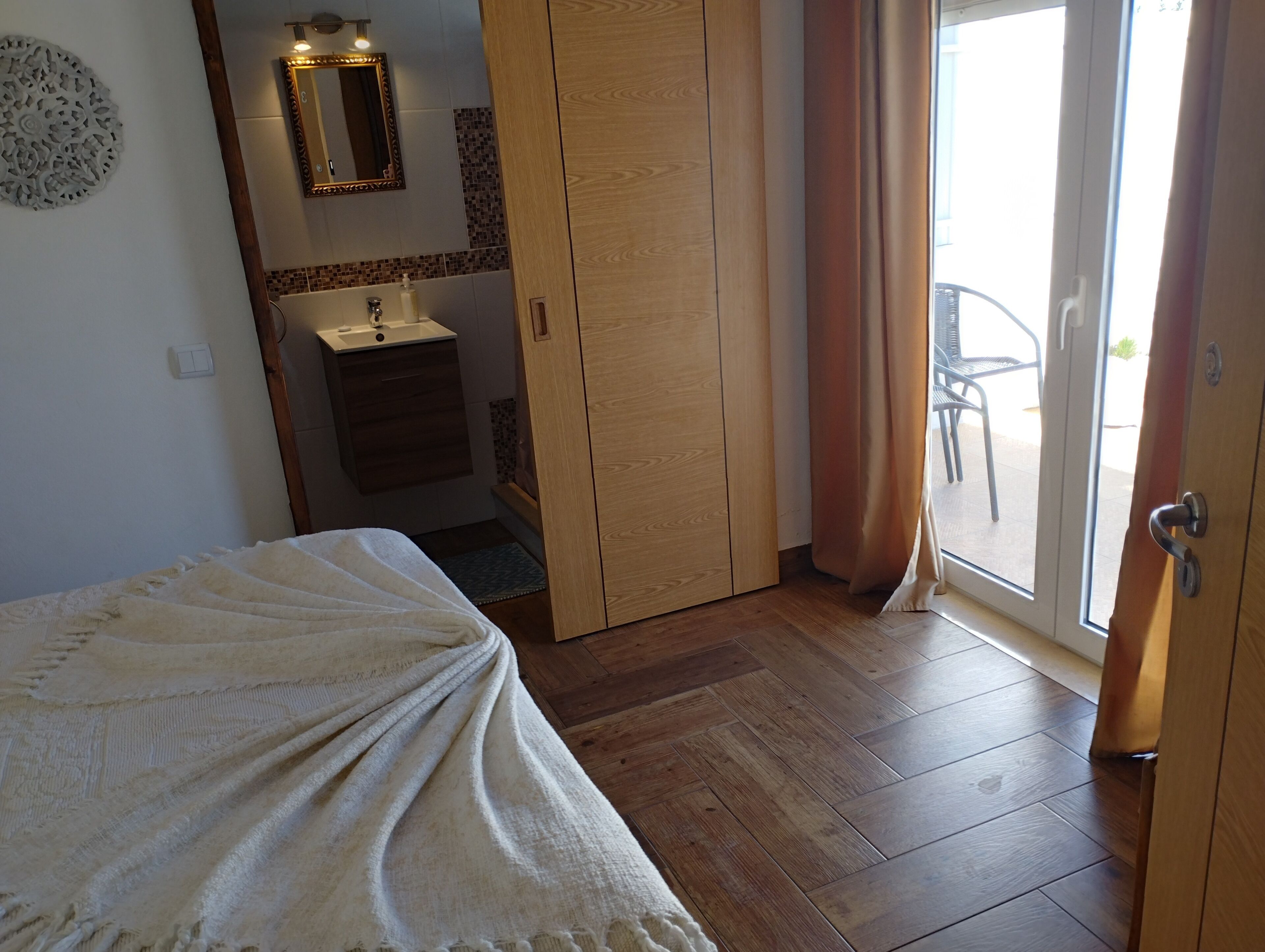 Ein Schlafzimmer mit einem Bett, einem Holzschrank, einem Badezimmer mit Waschbecken und Blick nach draußen durch eine Schiebetür.