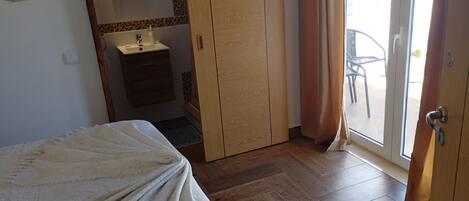 Ein Schlafzimmer mit einem Bett, einem Holzschrank, einem Badezimmer mit Waschbecken und Blick nach draußen durch eine Schiebetür.