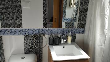 Un baño con lavamanos blanco, un espejo, inodoro y zona de ducha.