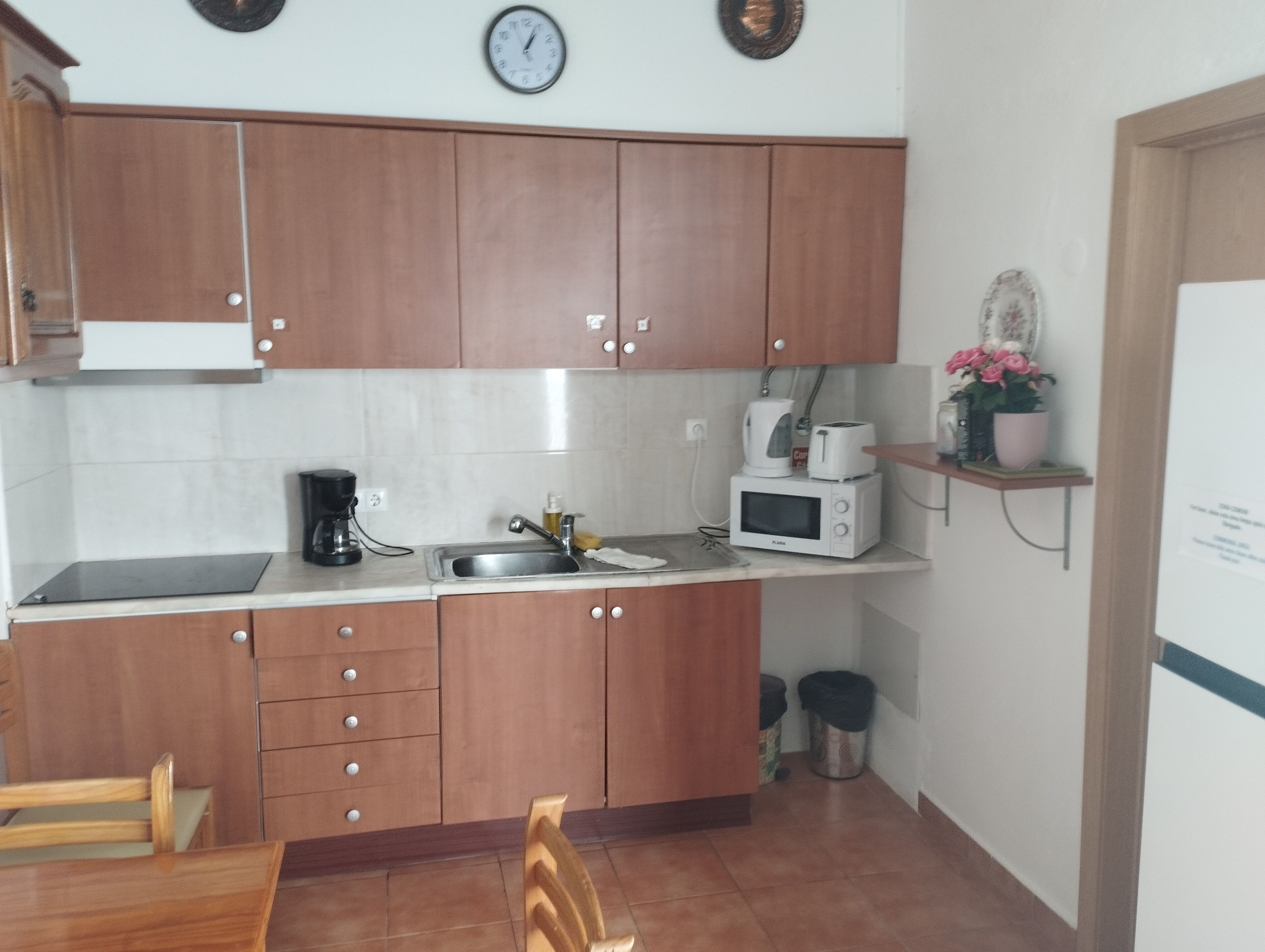 Een compacte keuken met houten kastjes, een magnetron, een koffiezetapparaat en een spoelbak.