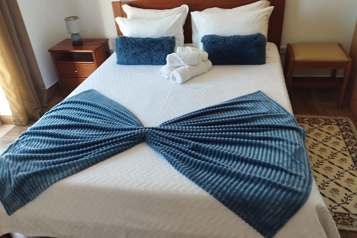 Una cama bien hecha con un edredón azul en forma de lazo, dos almohadas blancas y un cabecero de madera.