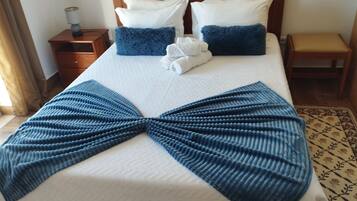 Una cama bien hecha con un edredón azul en forma de lazo, dos almohadas blancas y un cabecero de madera.