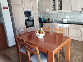 Eine Küche mit Holzausstattung, einer Mikrowelle, einem Backofen und einem Spülbecken. Es gibt einen Esstisch mit Stühlen und eine Fruchtkorb.