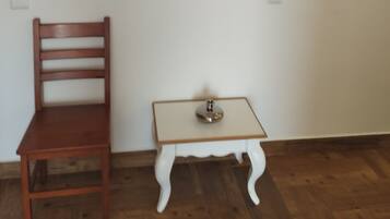 Una habitación con una silla de madera, una mesita con una lámpara y un cuadro enmarcado en la pared.