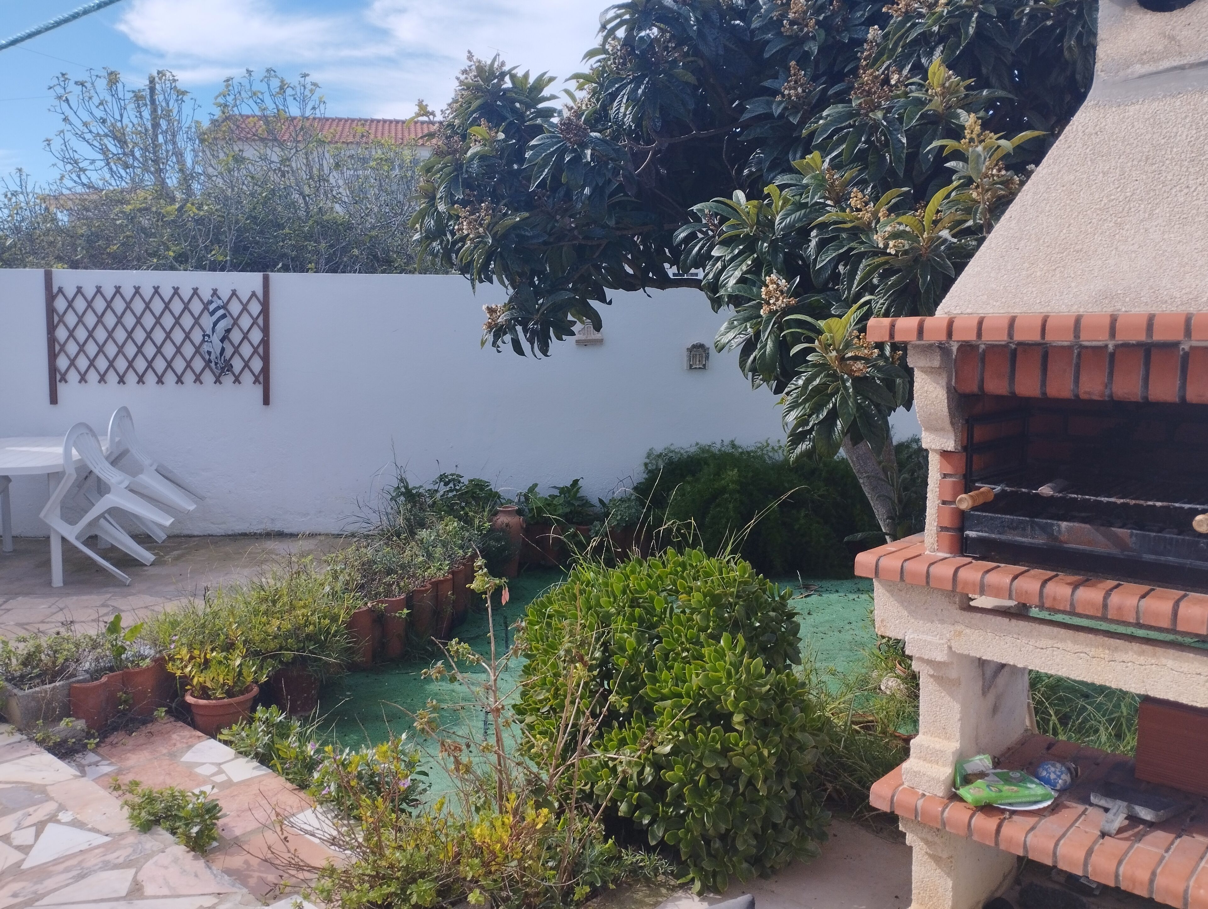A patio with a barbecue grill, potted plants, and a white wall with a lattice design.
