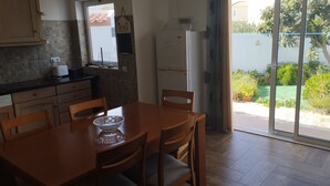 Une cuisine équipée d’une table et de chaises, d’un réfrigérateur et d’une fenêtre donnant sur un jardin.