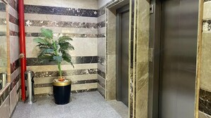 Un pasillo con pared de mármol, una planta en maceta, un cubo de basura y un ascensor.