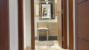 Un pasillo que conduce a una habitación con un armario espejado, un sillón acolchado y suelo de baldosas.