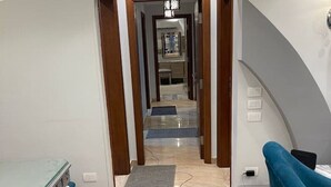Una habitación de hotel moderna con piso de mármol, sofá azul, mesa de vidrio y una araña.