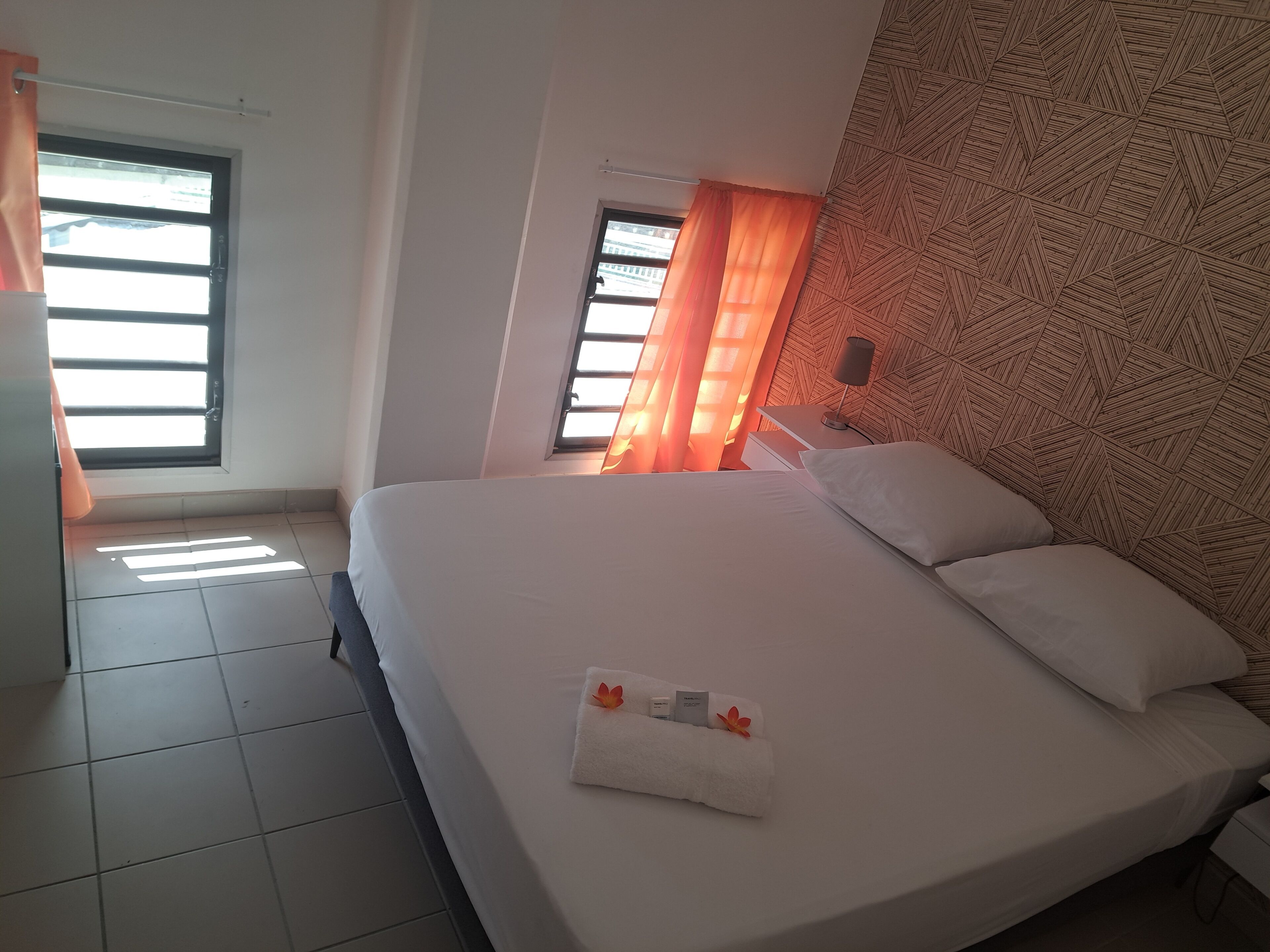 Habitación de hotel con una cama grande, una mesita de noche, una ventana con cortinas y un cabecero estampado.
