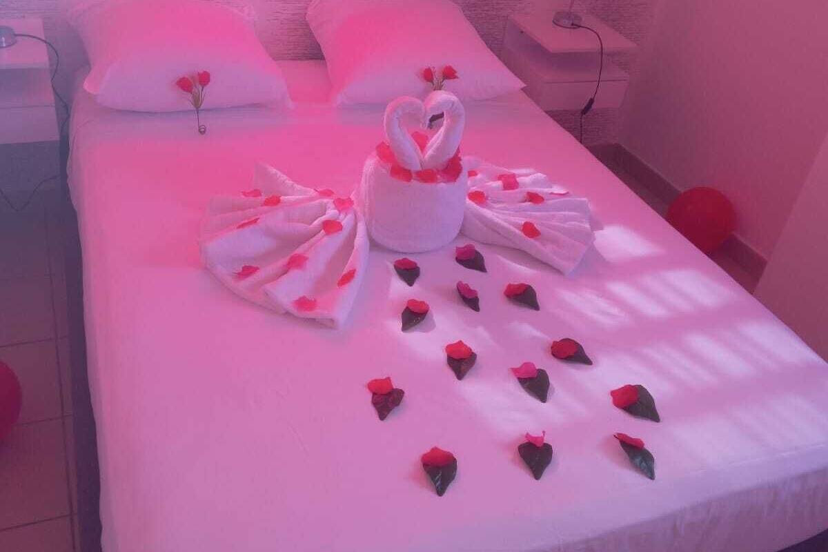 A hotel room with a bed, pillows, a nightstand, a lamp, and a window with curtains.