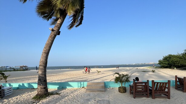 A beachside walkway leading to a sandy beach with palm trees, a clear blue sky, and a calm sea. - Cozy & Spacious 3BR Near Beach | Pool & Gym (Dar es Salaam)
