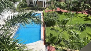 A view of a swimming pool surrounded by lush greenery and a multi-story building. - Cozy & Spacious 3BR Near Beach | Pool & Gym (Dar es Salaam)