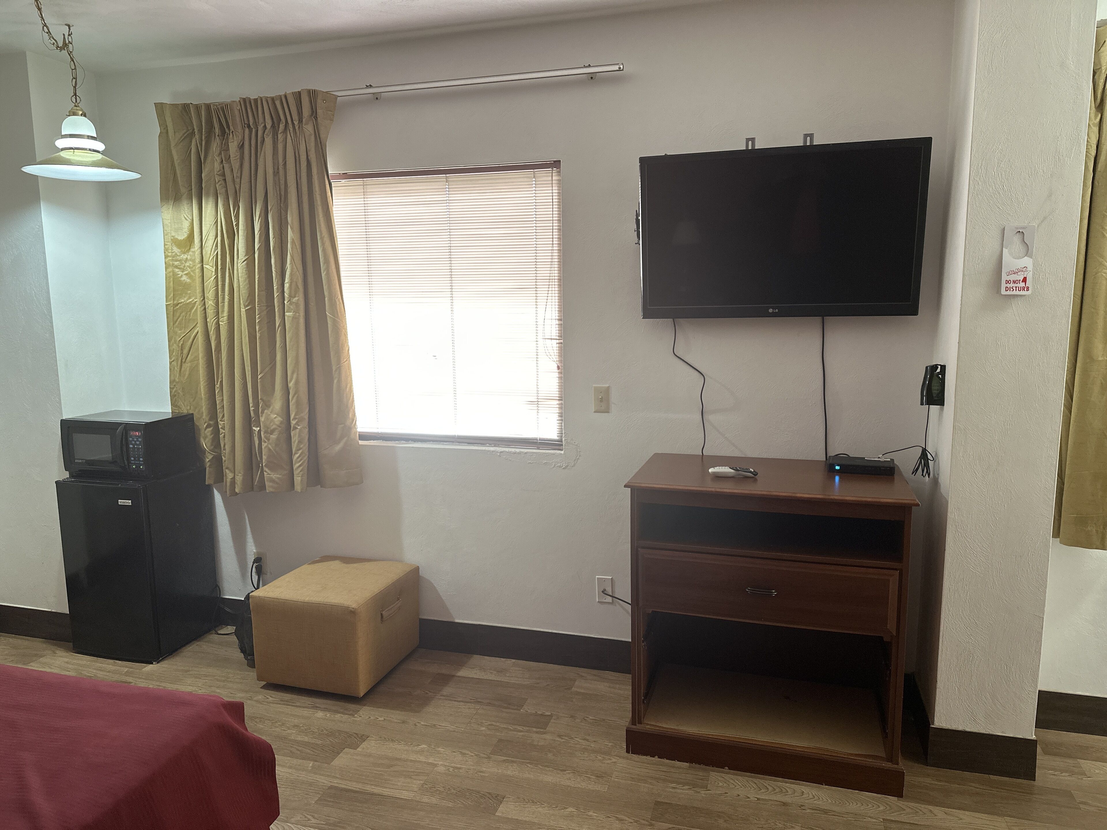 A hotel room with a flat-screen TV mounted on the wall, a small wooden desk with a computer, a microwave, and a refrigerator.