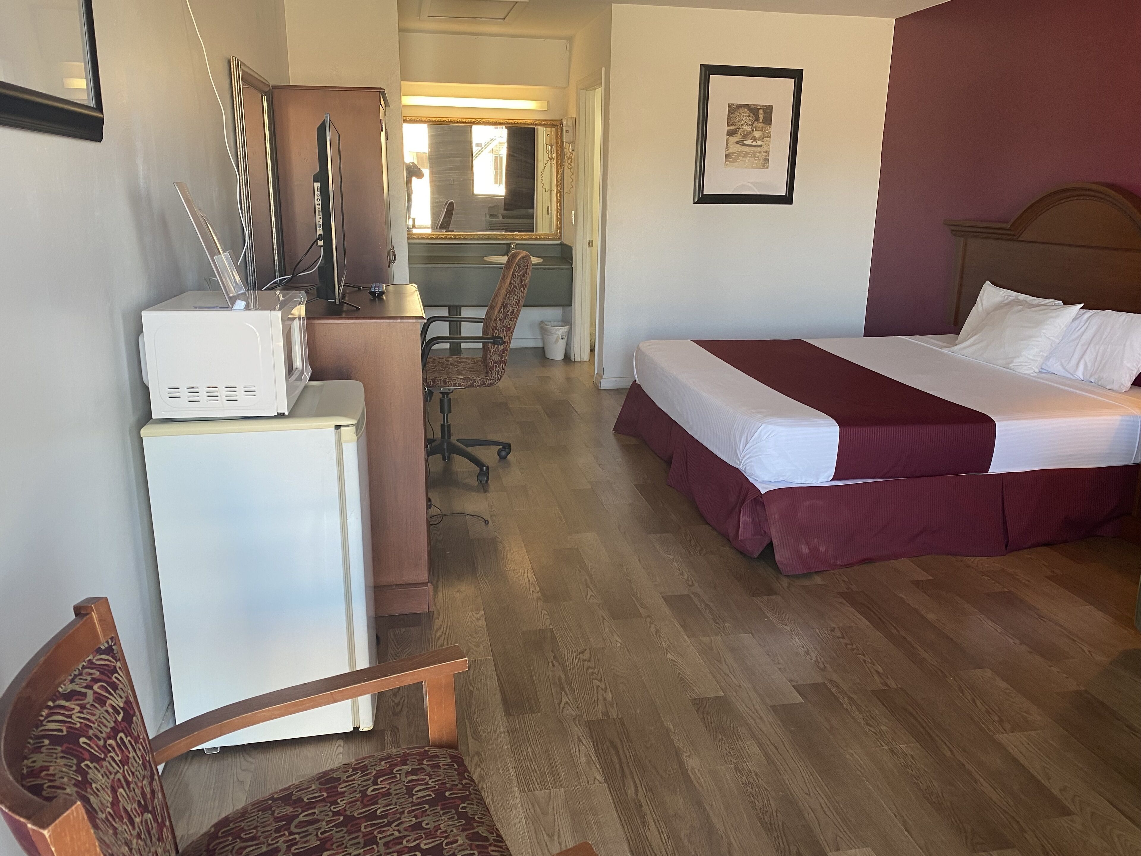 A hotel room with a bed, desk, chair, and a small kitchenette.