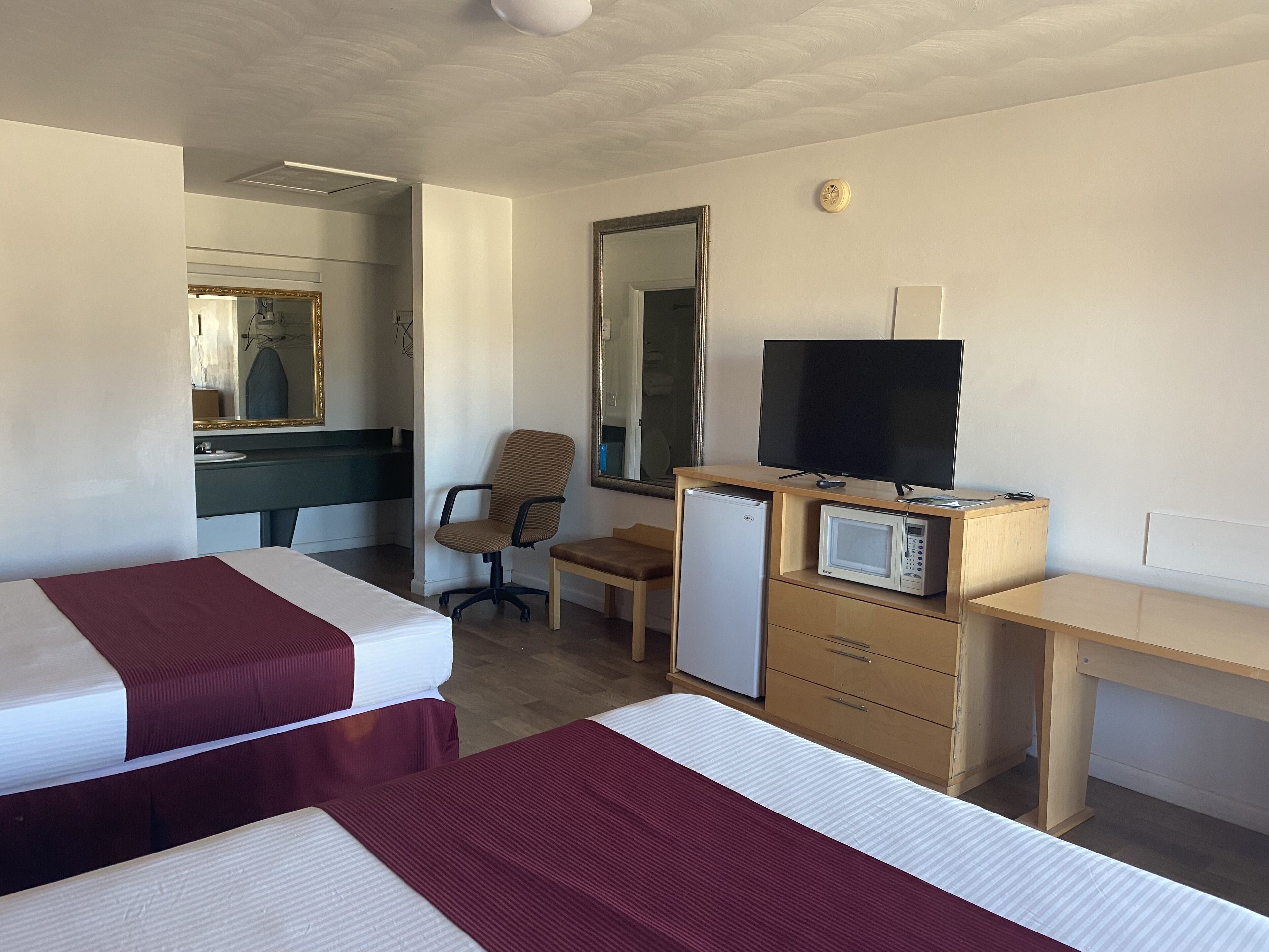A hotel room with two beds, a desk, a chair, a television, a microwave, and a refrigerator.
