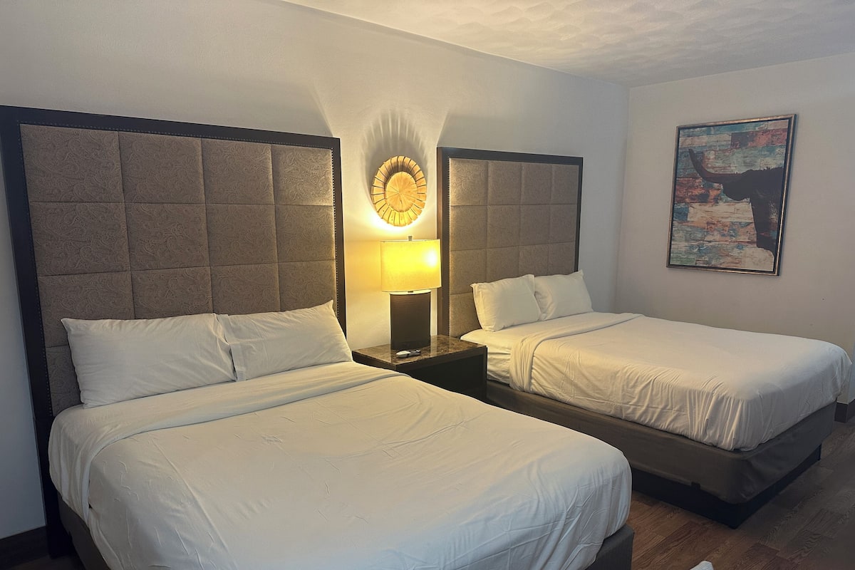 A hotel room with two beds, a nightstand with a lamp, and a painting on the wall.
