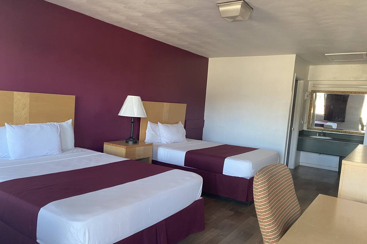 A hotel room with two beds, a nightstand with a lamp, a desk, and a mirror.