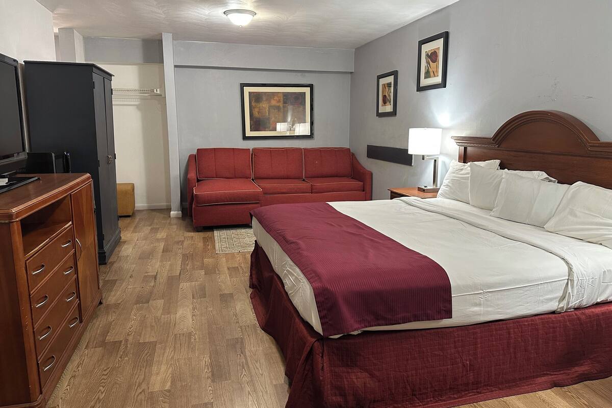 A hotel room with a bed, a wooden dresser, a red sofa, and a desk.
